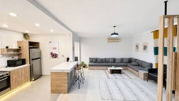A modern kitchen with a central island, a grey sectional sofa, and a wooden-framed partition.