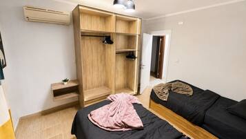 A bedroom with a wardrobe, two beds, a bedside table, and a hanging light fixture.