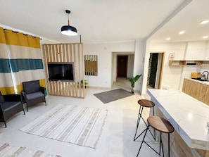 Uma sala de estar moderna com televisão, assentos e uma área de cozinha com balcão.
