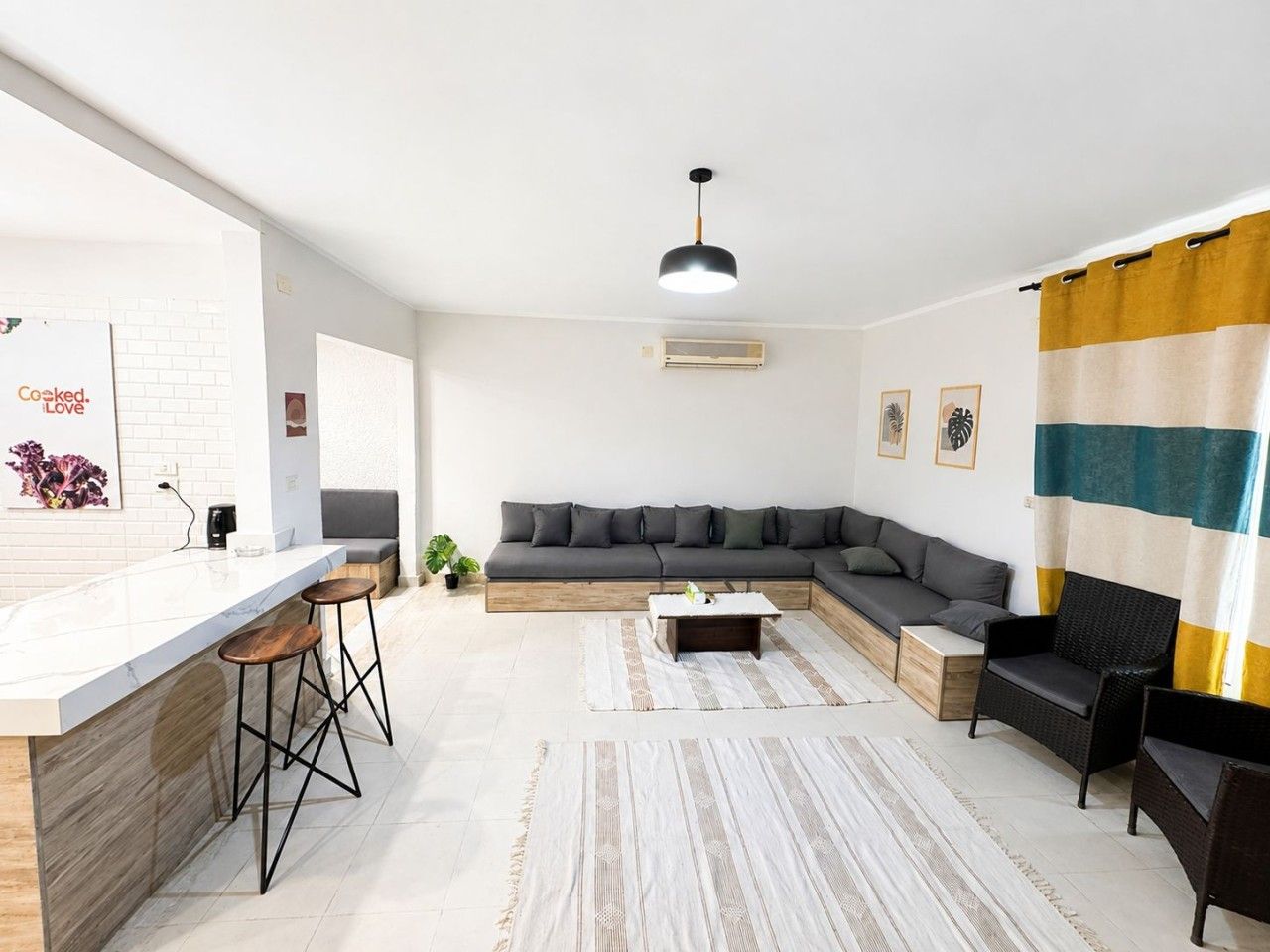 A modern living room with a kitchen area, a sofa set, a dining table, and a bar with stools.