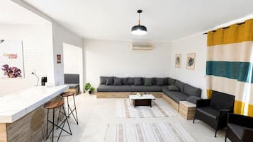 A modern living room with a kitchen area, a sofa set, a dining table, and a bar with stools.