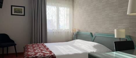 Hotellihuone, jossa on sänky, työpöytä, tuoli, ikkuna verhoilla ja kuvioitu seinä.