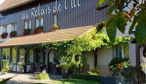 Un edificio con un letrero que dice 'Relais del M' y un área de estar al aire libre cubierta, con plantas en macetas y sillas.