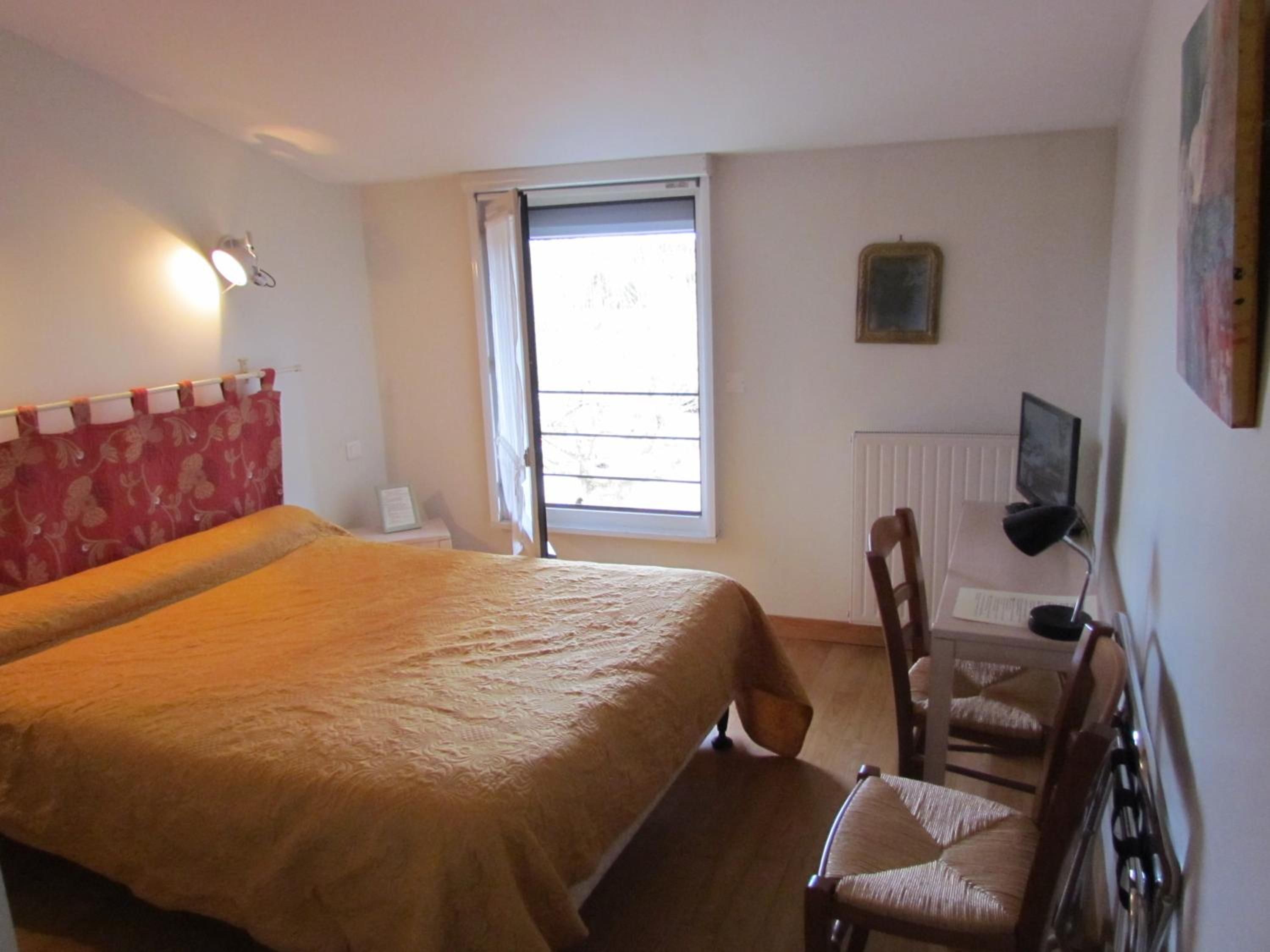 A bedroom with a bed, a chair, a television, and a window.