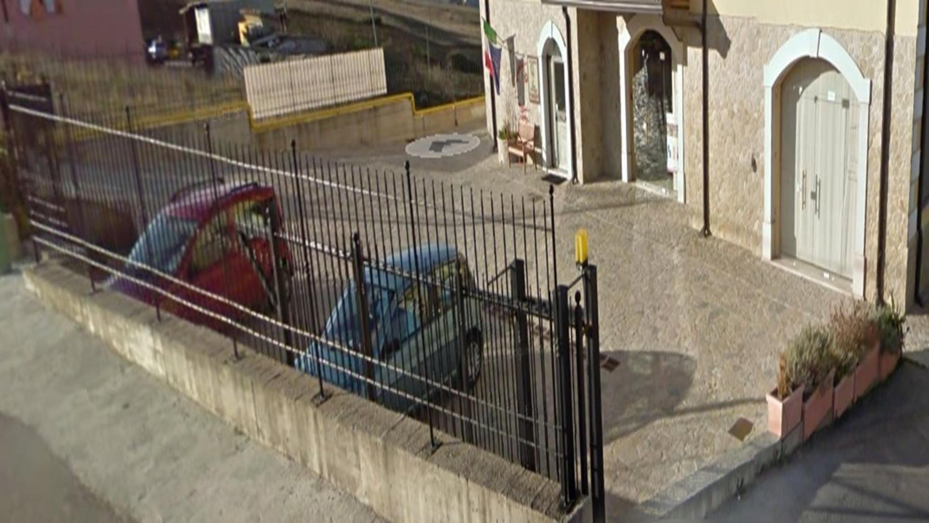 A fenced area with parked cars and a building with arched doorways.