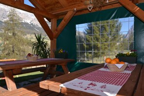 A wooden deck with a picnic table, a window with a view of mountains, and a potted plant. - Hotel Villa Gaia (Cortina d'Ampezzo)