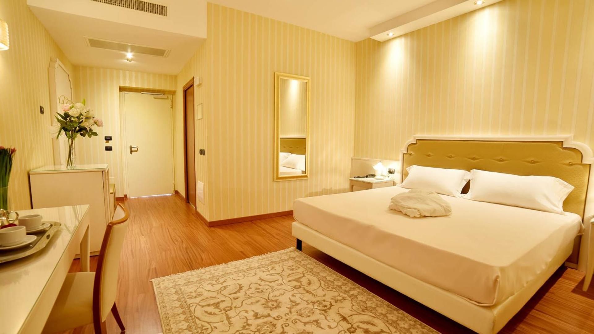 Una habitación de hotel con una cama, mesita de noche y espejo.