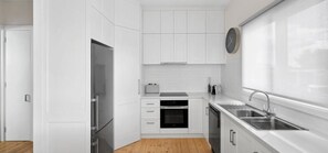 A compact kitchen with white cabinetry, a built-in oven, a sink, and a clock on the wall. - The Geelong West Gem (Greater Geelong)