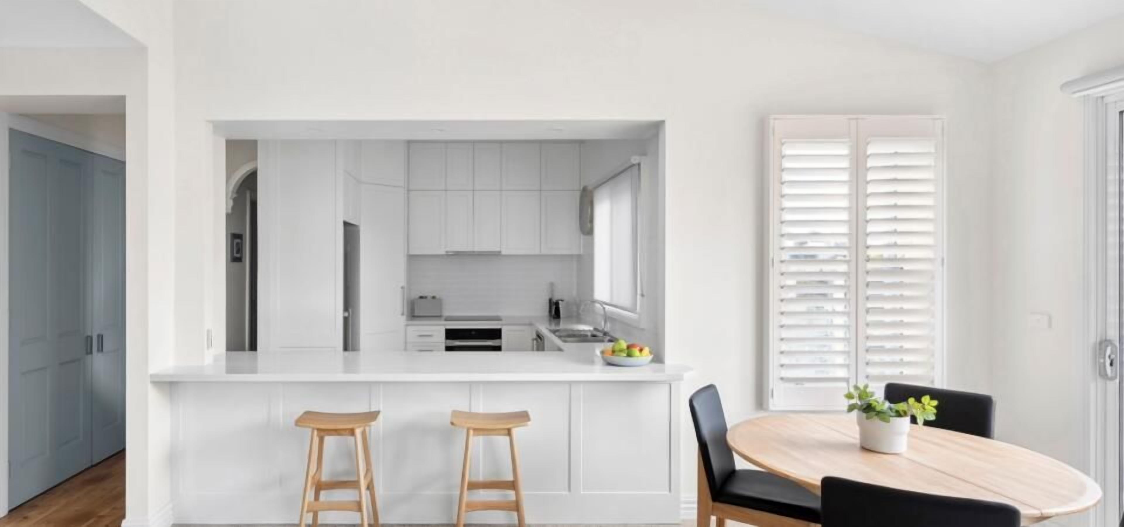 A modern kitchen with white cabinetry, a central island with stools, and a dining table with chairs.