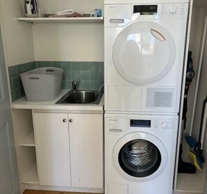 A compact laundry area with a stacked washer and dryer, a sink, and a basket. - The Geelong West Gem (Greater Geelong)