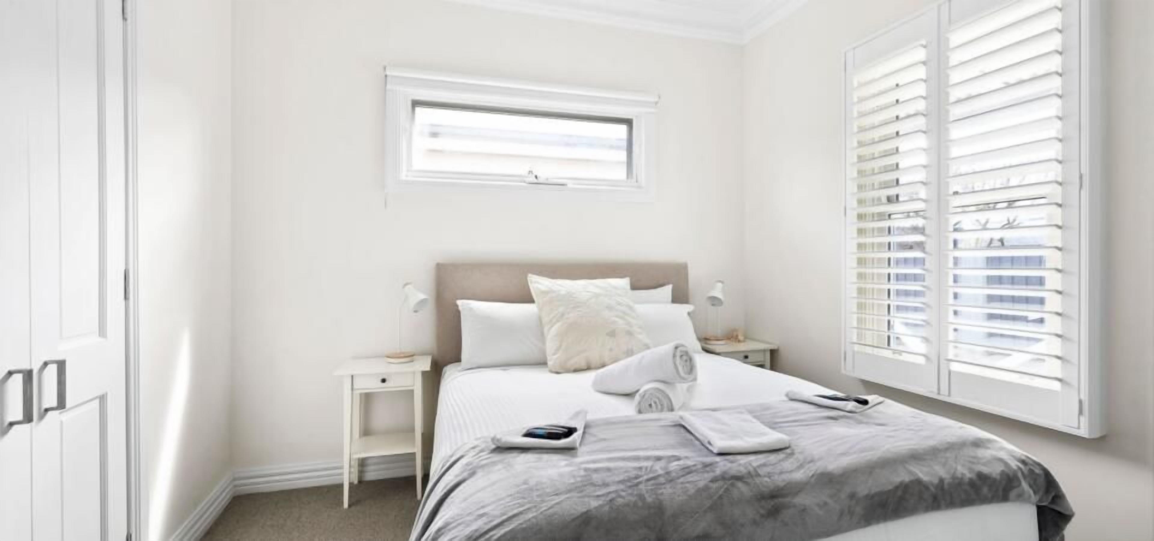 Una camera da letto con un letto, comodini, una finestra con persiane e una porta.