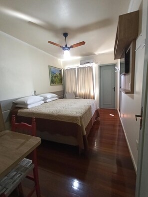 Ett hotellrum med en säng, ett skrivbord, en stol, en takfläkt, en tavla och en dörr.