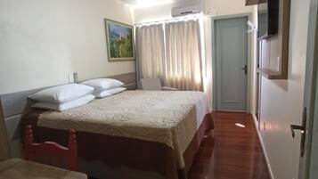 Quarto de hotel com cama, escrivaninha, cadeira, ventilador de teto, quadro e porta.