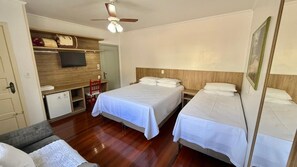 Ett hotellrum med en säng, ett skrivbord, en stol, en tv och en takfläkt.