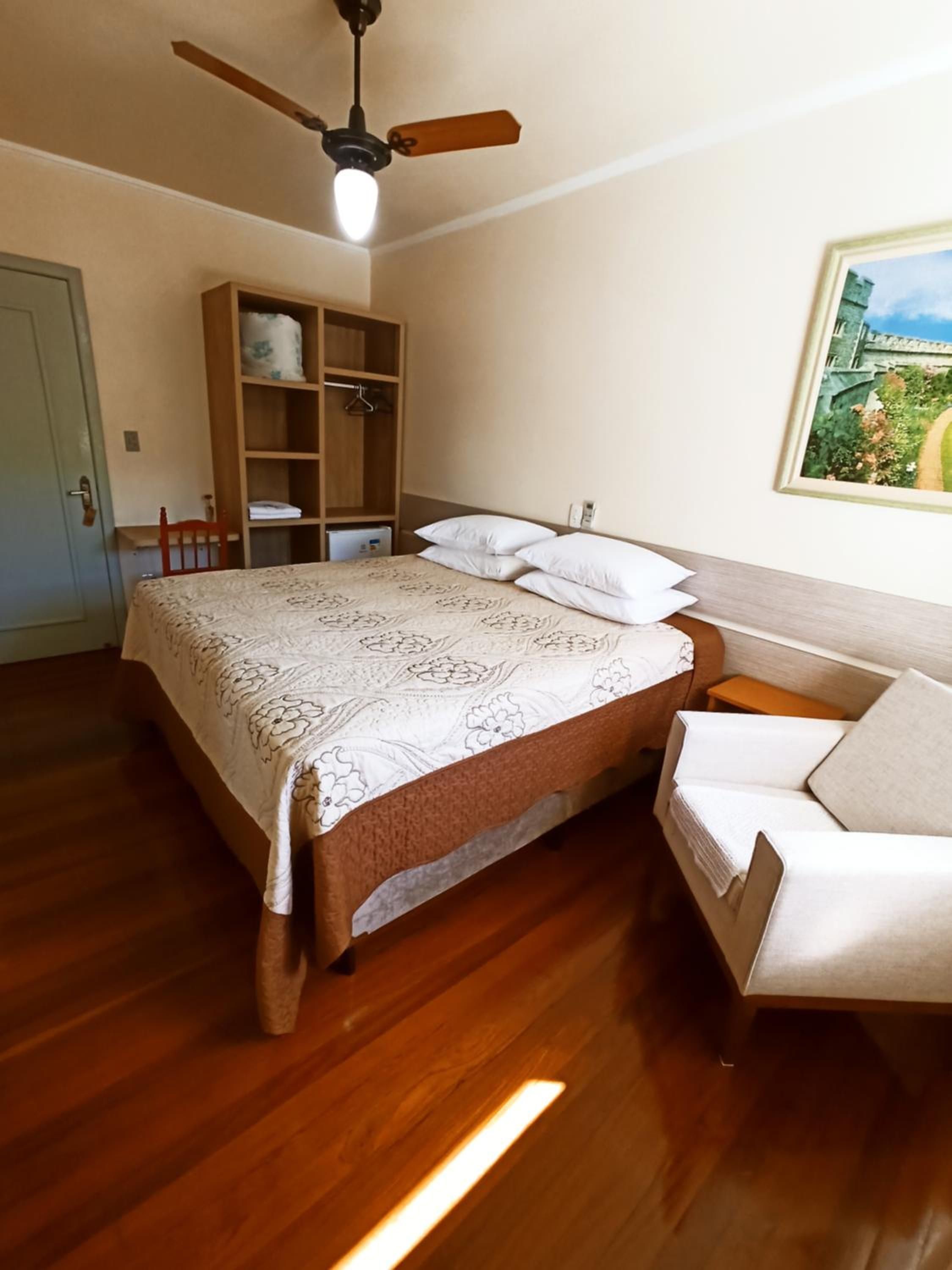 Un dormitorio con cama, armario de madera, ventilador de techo y un cuadro en la pared.