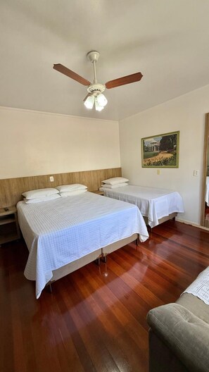 Ett hotellrum med två sängar, en takfläkt, en tavla på väggen och trägolv.