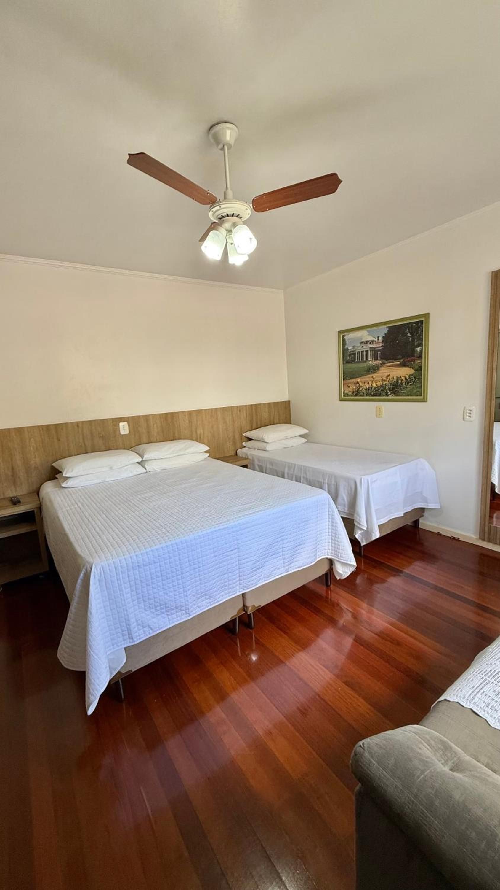 Habitación de hotel con dos camas, ventilador de techo, un cuadro en la pared y suelo de madera.