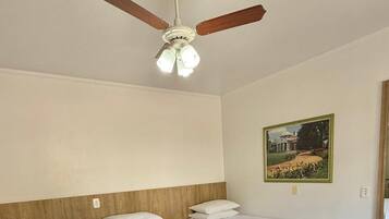 Habitación de hotel con dos camas, ventilador de techo, un cuadro en la pared y suelo de madera.