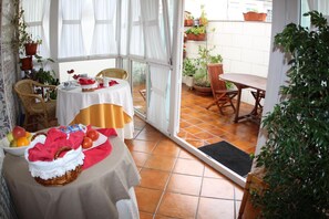 Un comedor con una mesa lista para dos, una silla de mimbre y vistas del patio con plantas en macetas.