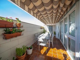 Eine sonnendurchflutete Terrasse mit gefliestem Boden, einem weißen Tisch mit Stühlen und Topfpflanzen an der Wand.