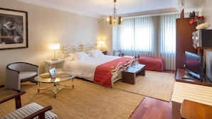 A hotel room with a bed, bedside tables, a television, a chair, a small table, and a window with curtains. - El Descanso De Wendy (Astorga)