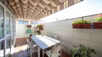 Un patio con mesa y sillas, un jardín colgante y piso de baldosas.