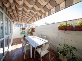 Un patio con mesa y sillas, un jardín colgante y piso de baldosas.