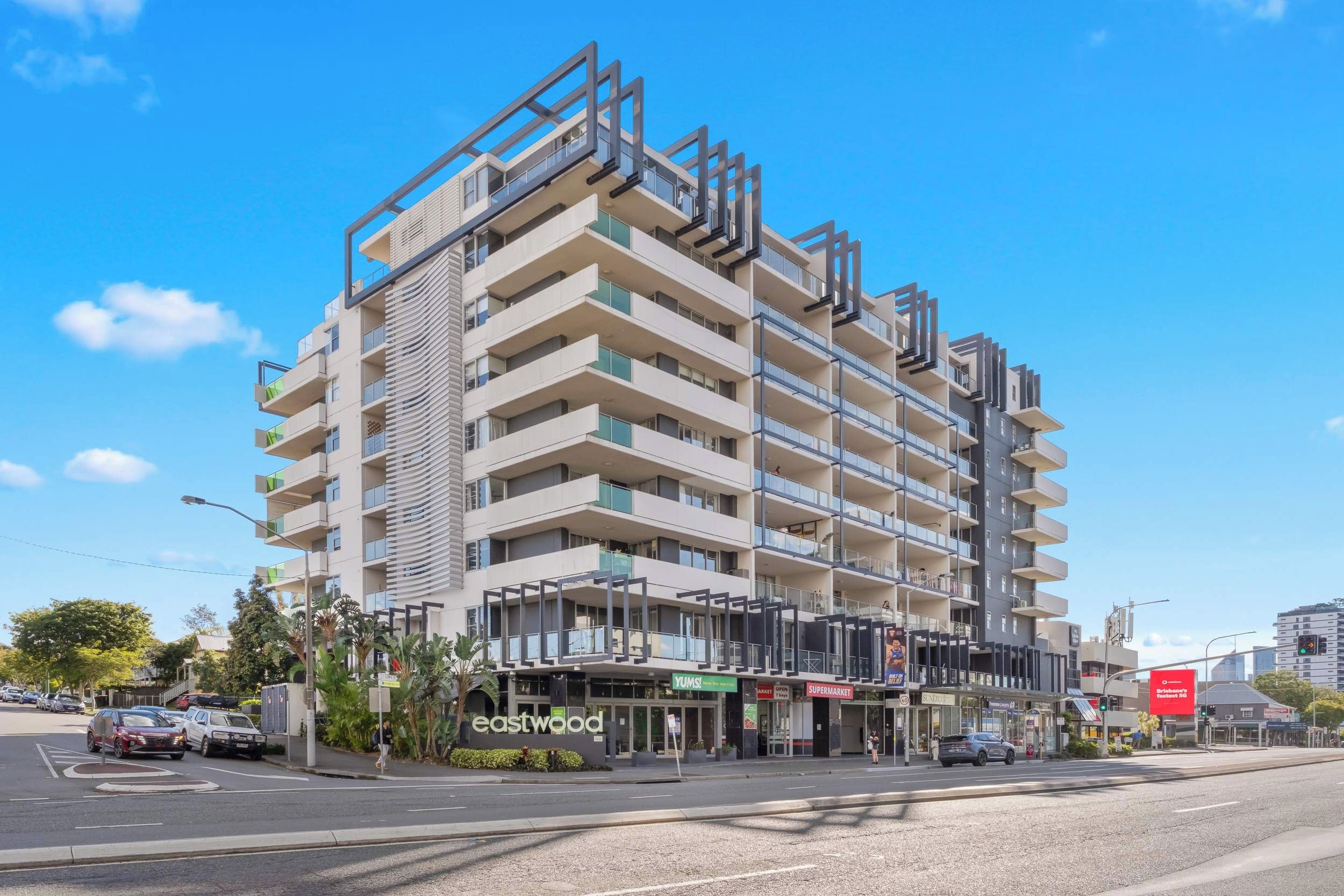 Ein mehrgeschossiges Gebäude mit moderner Architektur, das Balkone und einen Erdgeschossbereich mit Geschäften aufweist.
