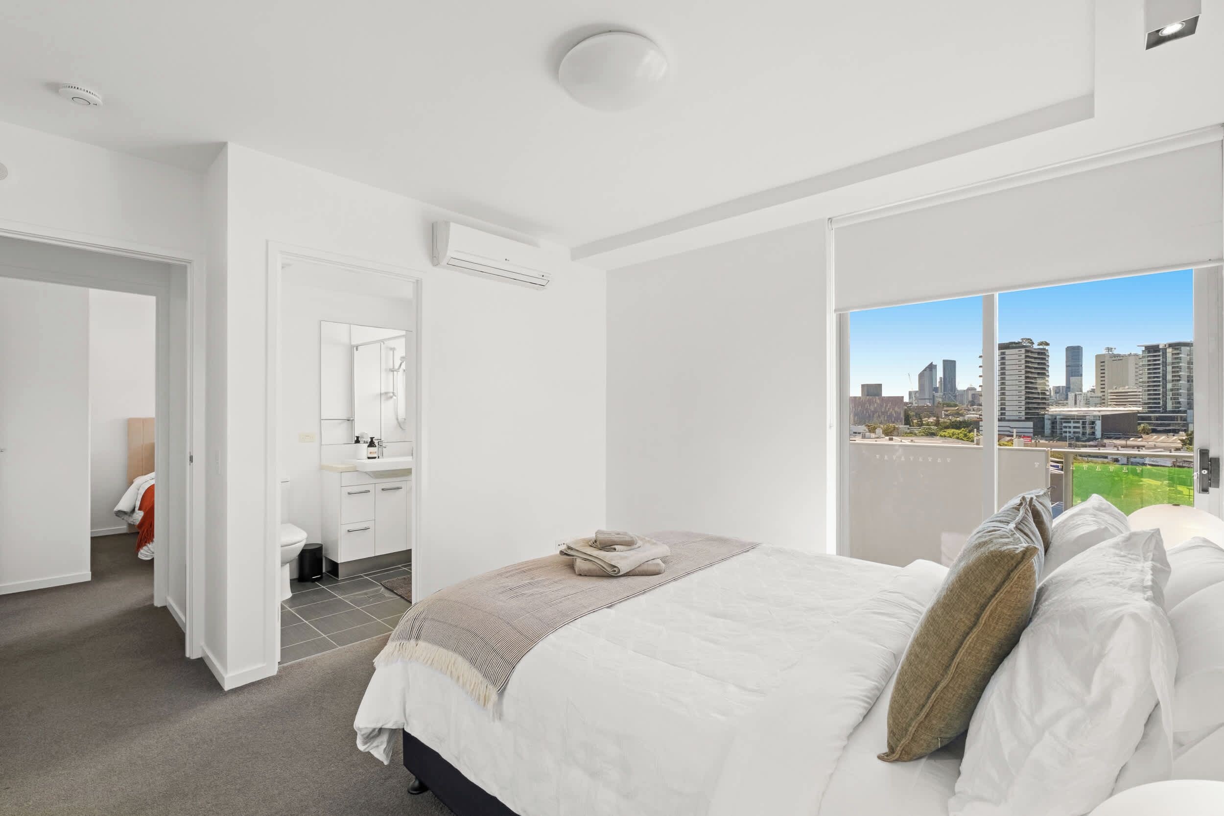 A modern bedroom with a city view, a large bed, and a walk-in closet.