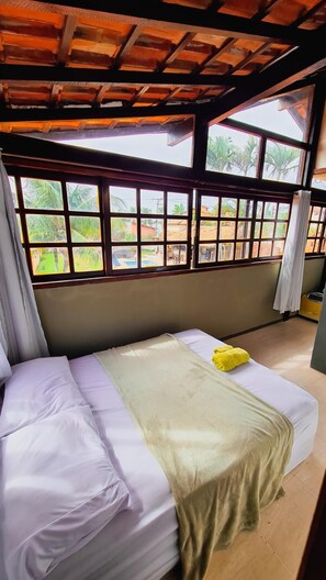 A room with a bed, large windows, and a view of greenery outside. - Hostel Lagoa Do Sol (Saquarema)