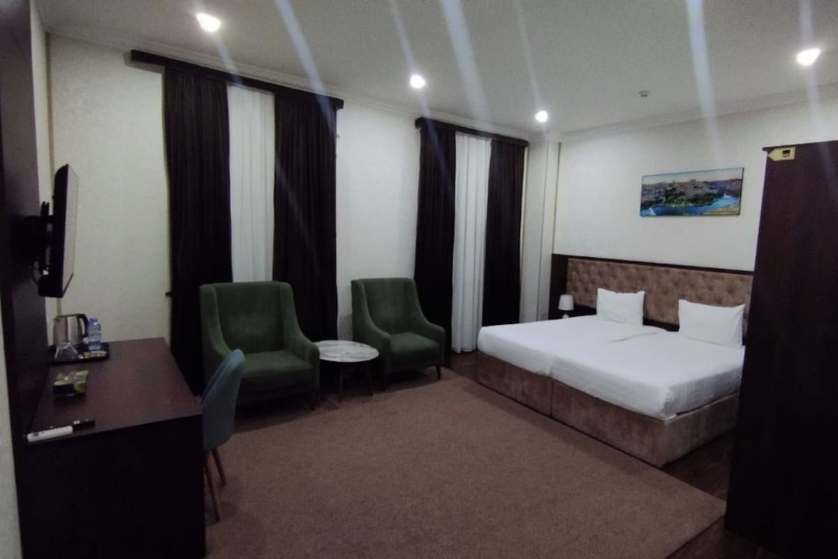 A hotel room with a bed, two chairs, a small table, a TV, and a painting on the wall.