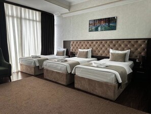 A hotel room with a large bed, two smaller beds, a chair, a painting on the wall, and a window with curtains. - Toshkent Grand Turon 1 (Tashkent)