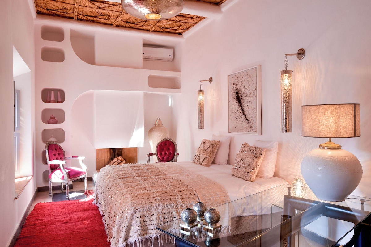 Un dormitorio moderno con una cama grande, una alfombra roja, una mesa de centro de cristal y una chimenea.