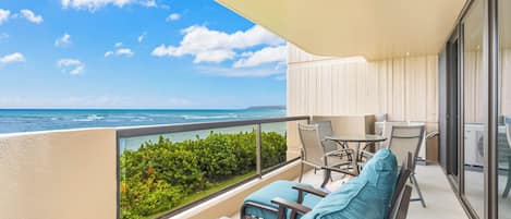 Un balcon avec vue sur l’océan, un coin salon avec des chaises et une table, et une porte vitrée donnant sur l’intérieur.