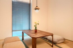 A room with a wooden table, a vase with flowers, a hanging light, and a window with blinds. - NIKYO DonHaus Private Villa OSAKA (Osaka)