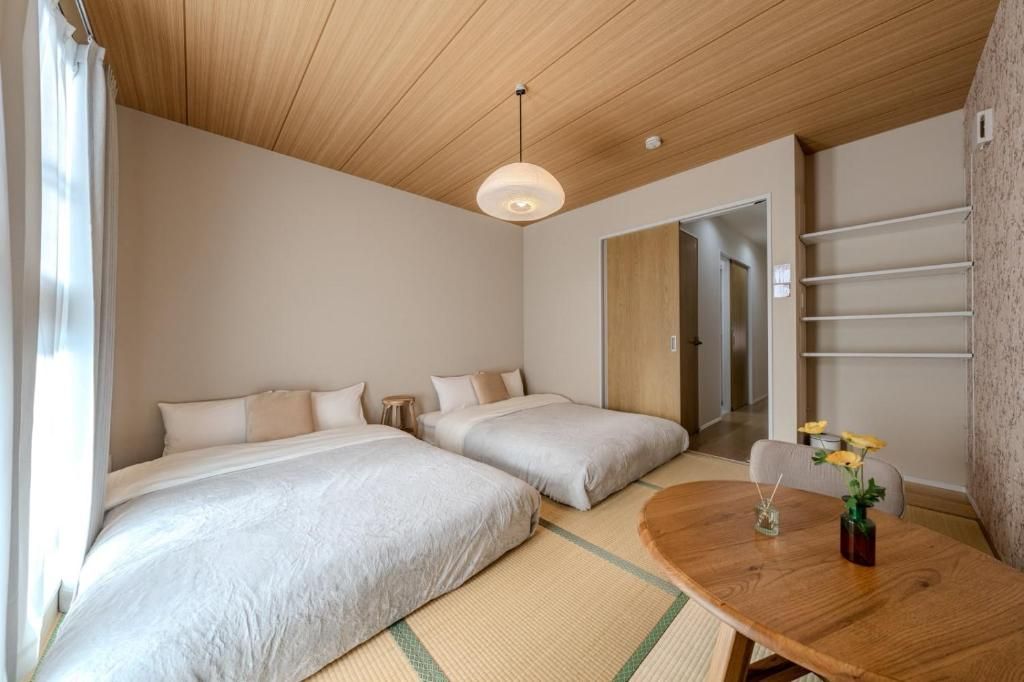 A hotel room with two beds, a wooden ceiling, a round dining table, and a small table with flowers.