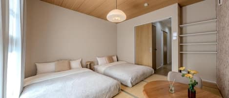 A hotel room with two beds, a wooden ceiling, a round dining table, and a small table with flowers.