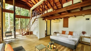 A spacious room with a large bed, a sofa, a dining table, and a staircase leading to an upper level. - Palm Paradise Cabanas Ltd (Tangalle)