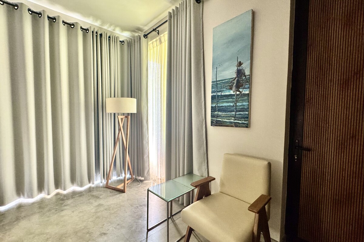 A room with a large window, a floor lamp, a chair, and a painting on the wall.