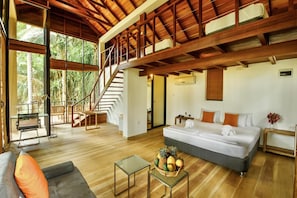 A spacious room with a large bed, a sofa, a dining table, and a staircase leading to an upper level.