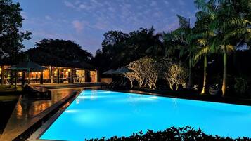 A swimming pool at dusk with surrounding palm trees and a building with outdoor seating.