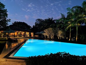 A swimming pool at dusk with surrounding palm trees and a building with outdoor seating.