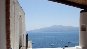 A balcony with a table and two chairs, overlooking a body of water with boats and a mountain in the distance. - Hotel Santa Marina Antica Foresteria (Santa Marina Salina)