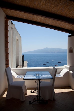 A balcony with a table and two chairs, overlooking a body of water with boats and a mountain in the distance. - Hotel Santa Marina Antica Foresteria (Santa Marina Salina)