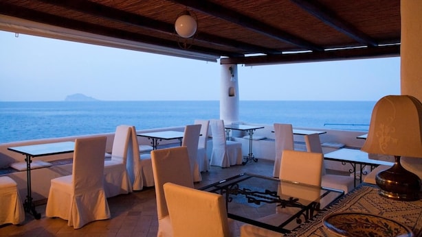 A covered outdoor seating area with tables and chairs, overlooking the sea. - Hotel Santa Marina Antica Foresteria (Santa Marina Salina)