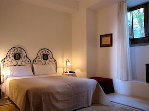 Habitación de hotel con cama, mesita de noche, lámpara y ventana con cortinas.