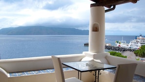 A balcony with a glass table and two chairs, overlooking a body of water and a distant island. - Hotel Santa Marina Antica Foresteria (Santa Marina Salina)
