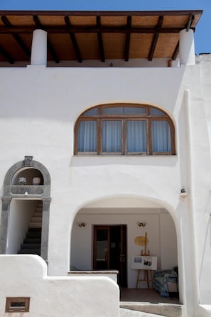 Un edificio de dos pisos con fachada blanca, un balcón de madera y una pequeña entrada en arco.