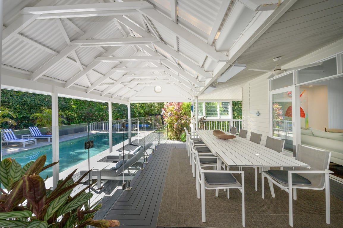 A covered outdoor area with a pool, lounge chairs, and a dining table.
