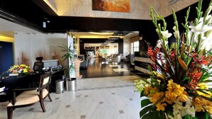 En hotellobby med en receptionsdisk, en sittgrupp och en stor blomsterdekoration.
